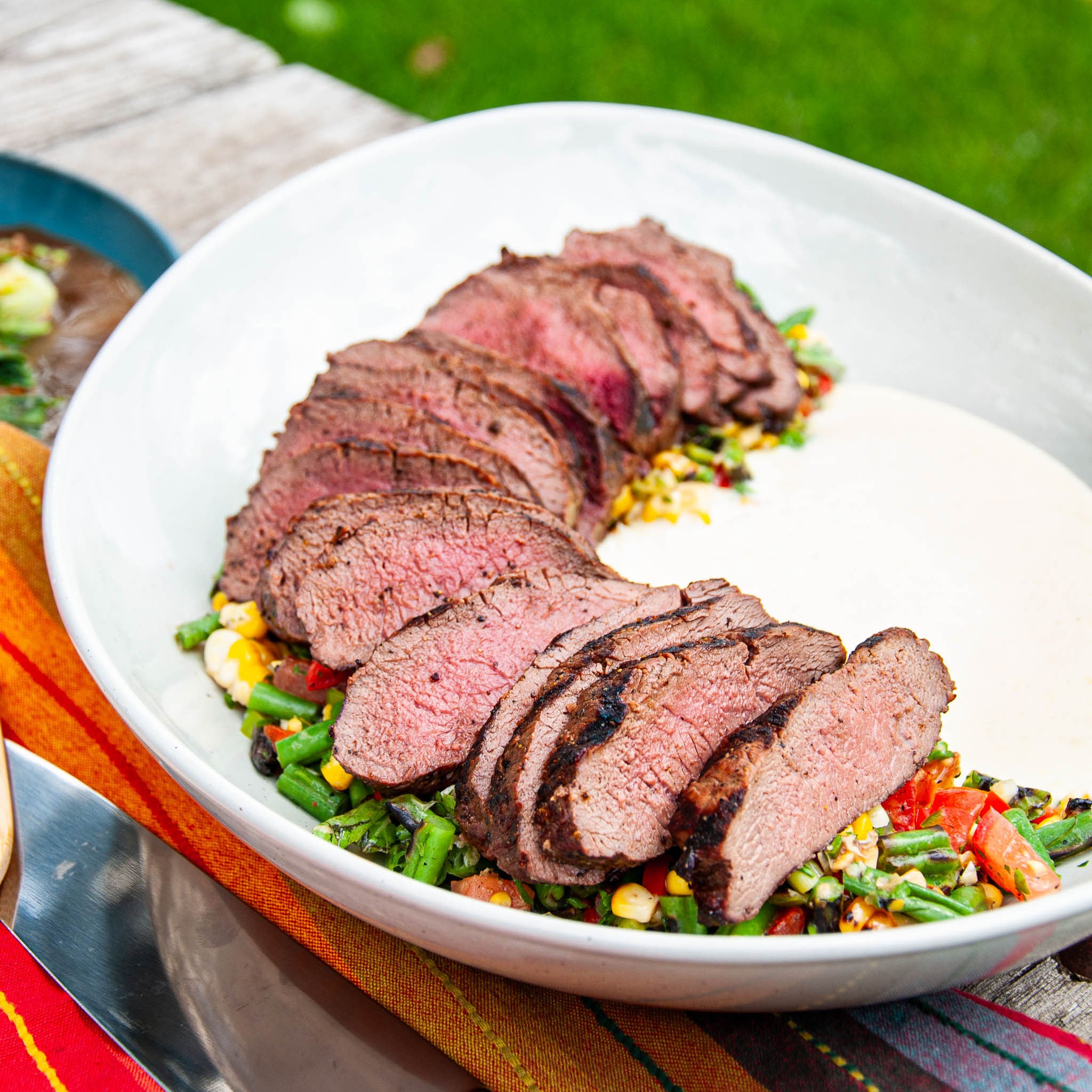 Sliced steak on a bed of vegetables in a white bowl with a grassy background