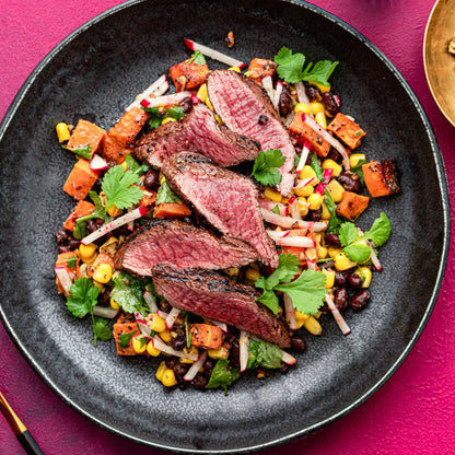 Plated dish of sliced steak with a colorful side salad on a pink background