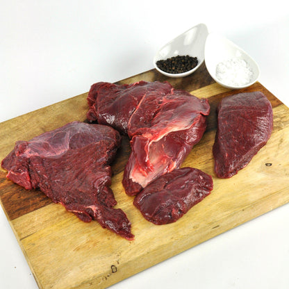Raw beef on a wooden cutting board with salt and pepper shakers.