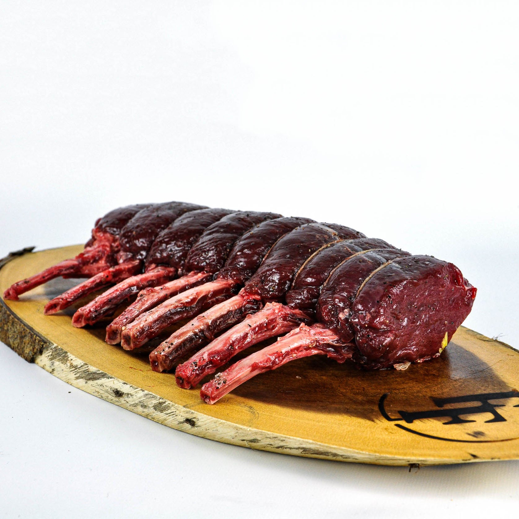 Raw rack of lamb on a wooden cutting board with a white background