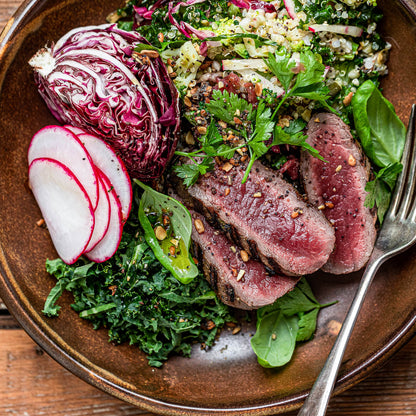Plated dish with sliced beef, radicchio, and greens on a wooden surface