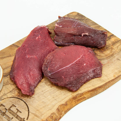 Three pieces of raw beef on a wooden cutting board with a brand logo.