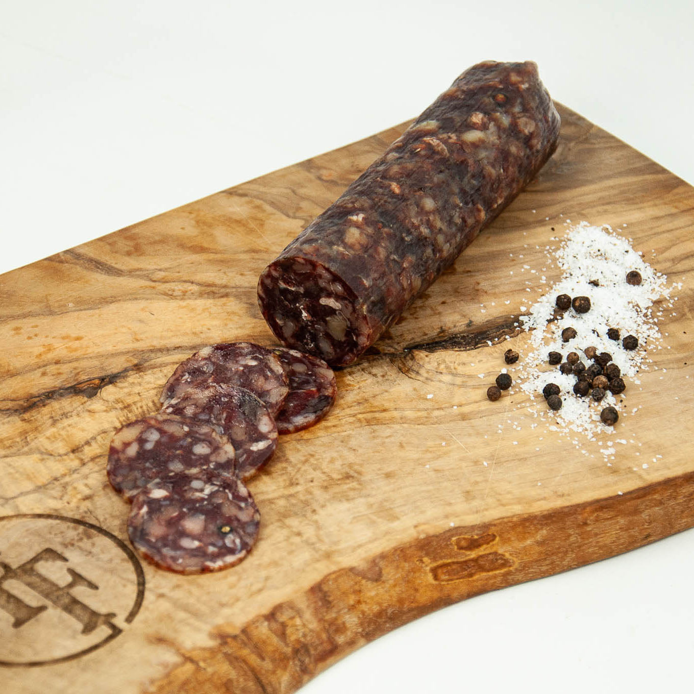Rolled salami with slices on a wooden cutting board with salt and pepper.