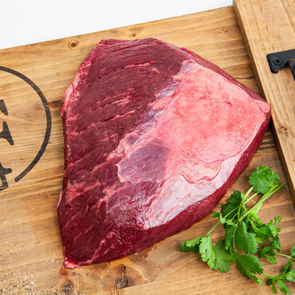 Raw beef brisket on a wooden cutting board with fresh herbs