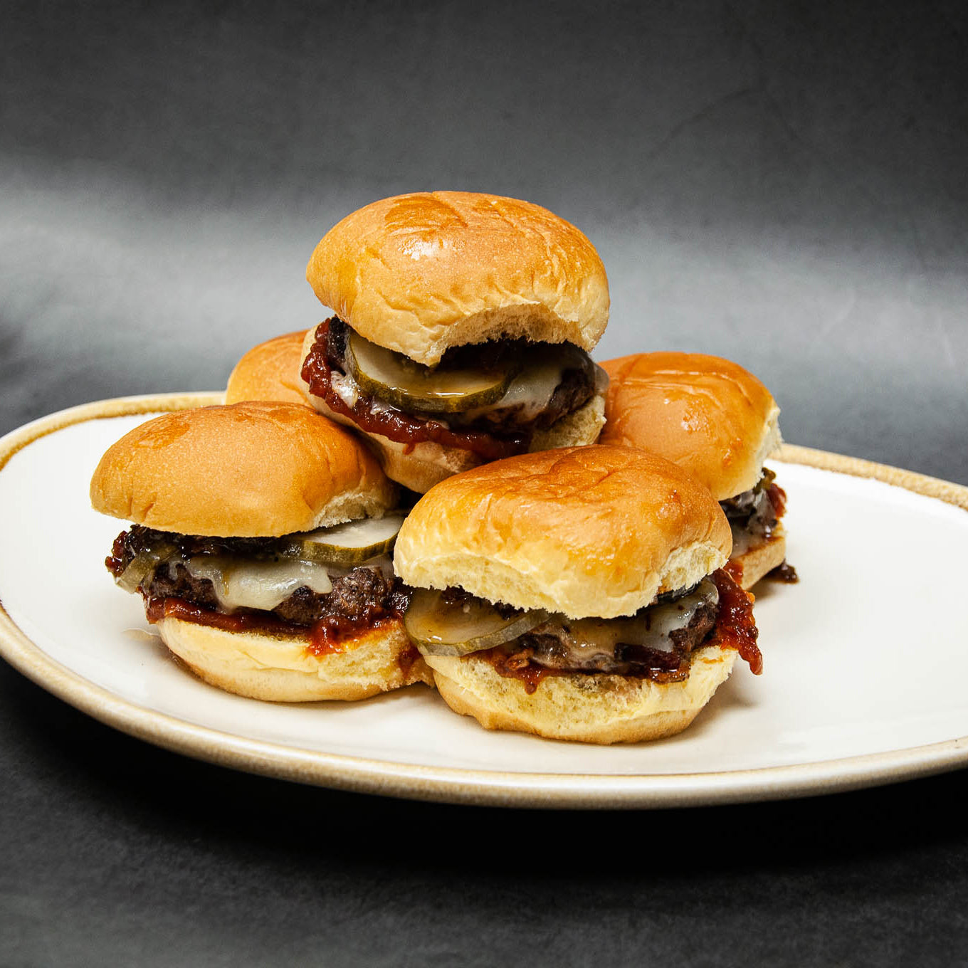 Stack of mini burgers on a white plate with a dark background