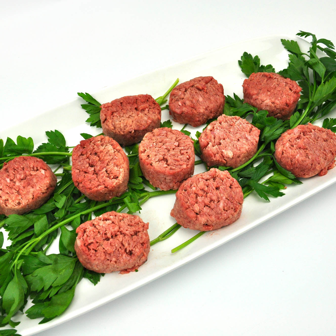 Raw ground meat patties on a bed of greens on a white plate