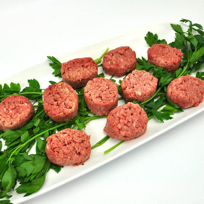 Raw ground meat patties on a bed of greens on a white plate