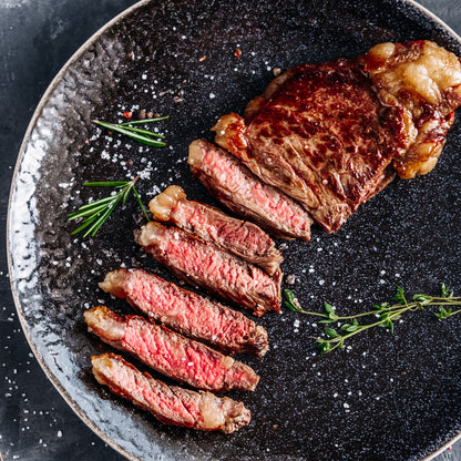 Sliced steak on a black plate with herbs