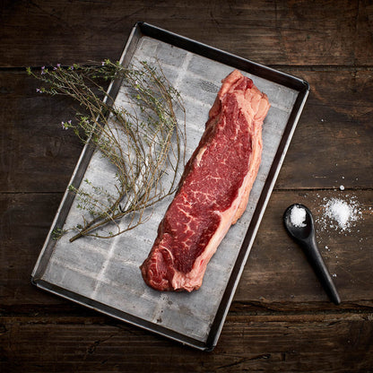 Raw steak on a metal tray with herbs and salt on a wooden surface