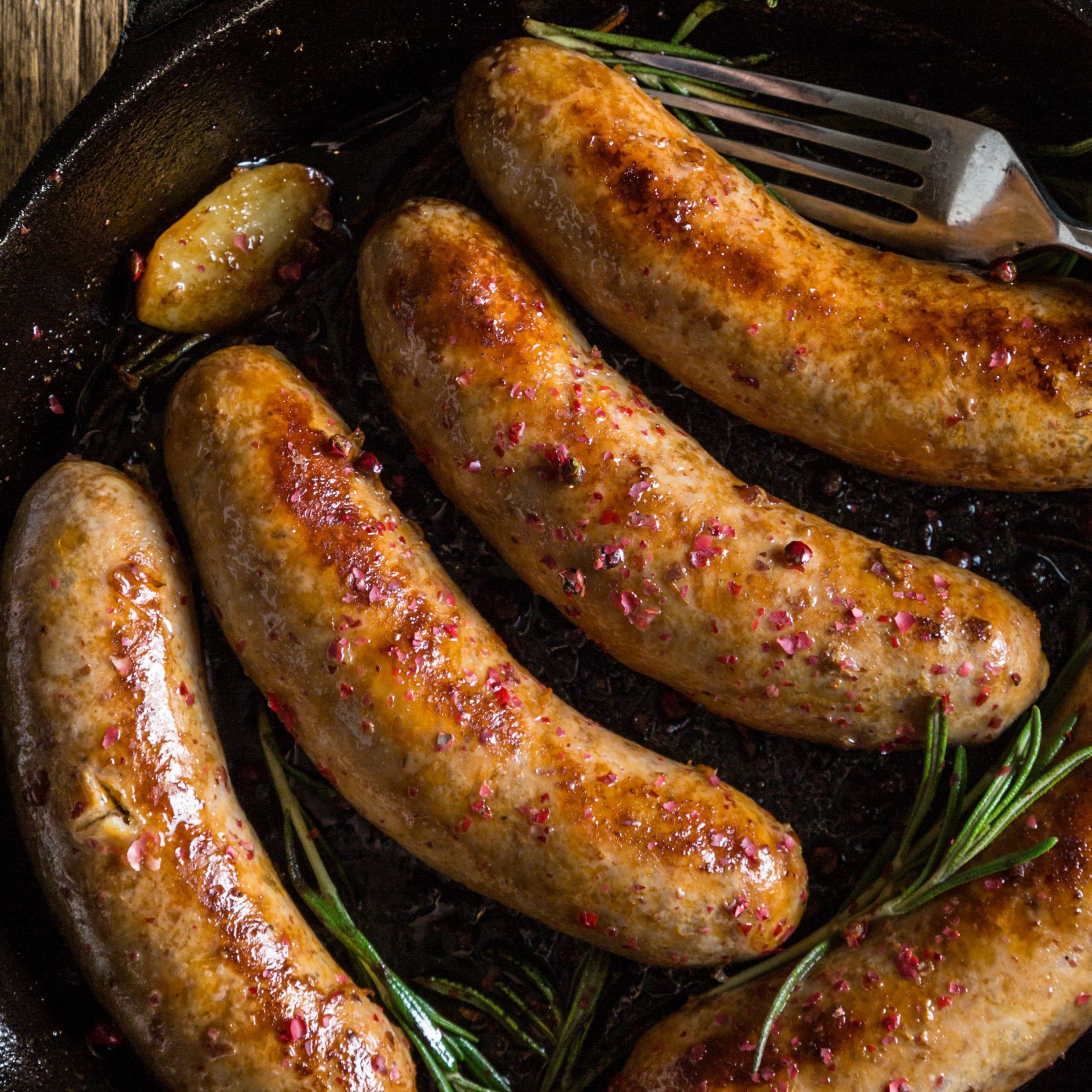 Sausages cooking in a pan with rosemary sprigs