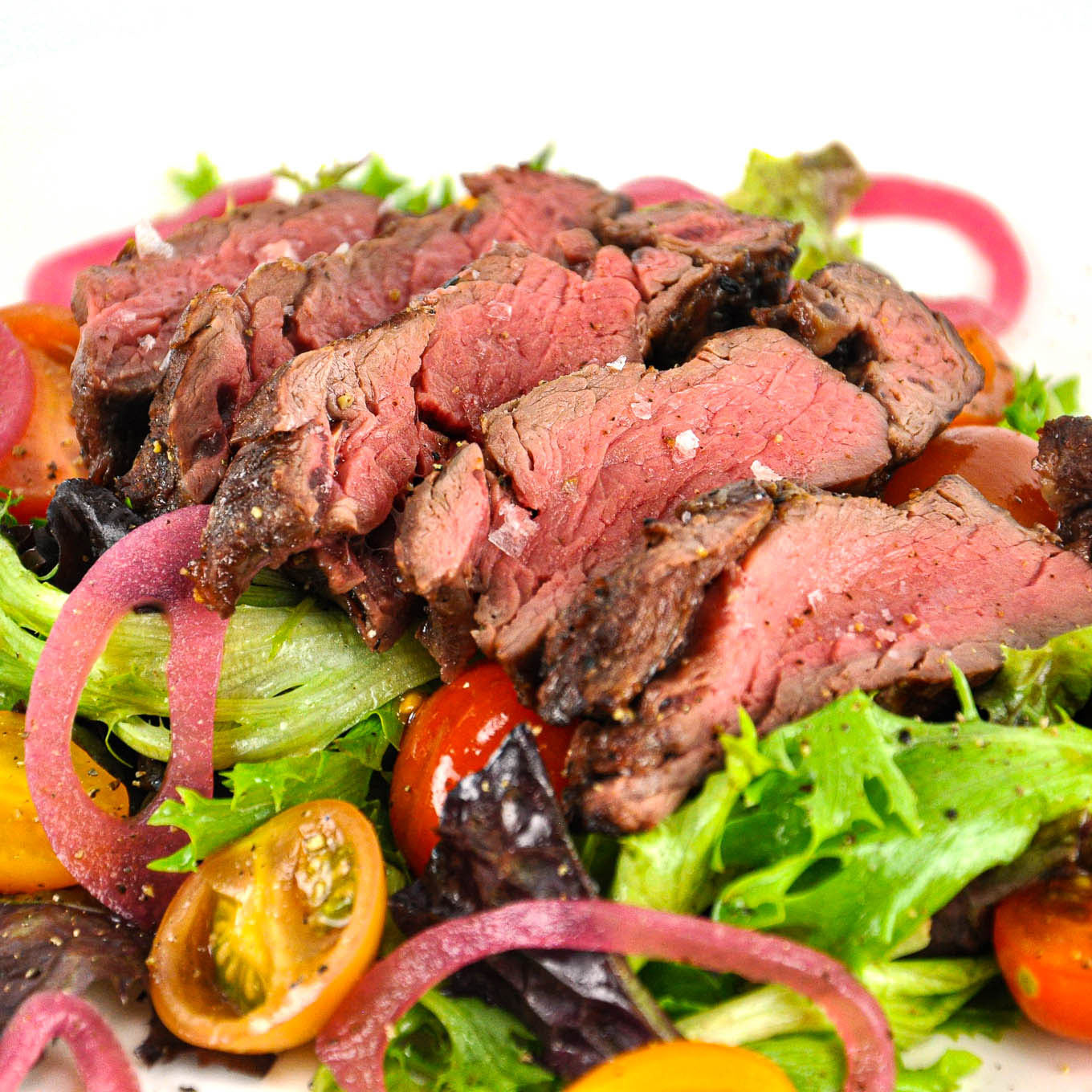 Steak salad with sliced beef, lettuce, tomatoes, and red onions on a white background