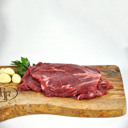 Raw beef on a wooden cutting board with garlic and parsley on a white background