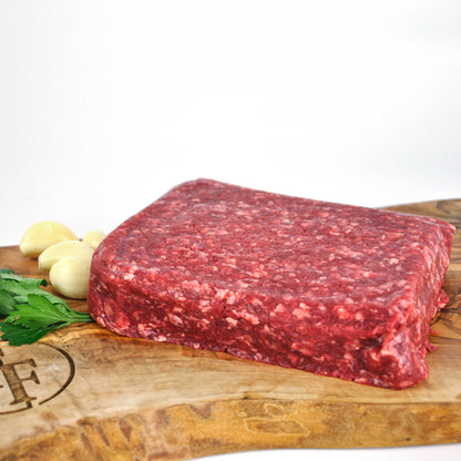 Raw ground beef on a wooden cutting board with garlic and parsley.