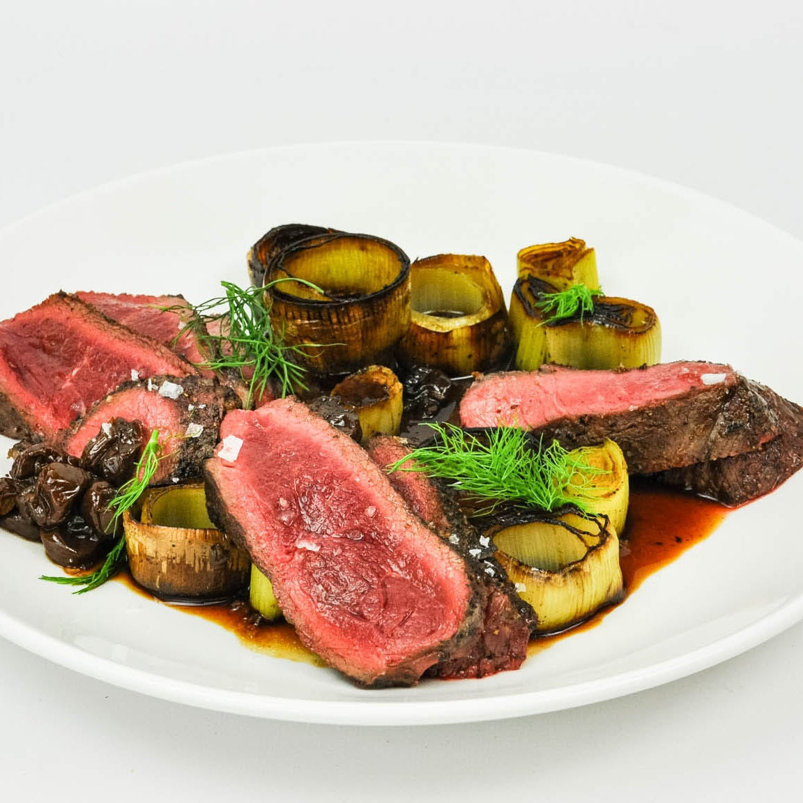 Plated dish of sliced beef with vegetables on a white background
