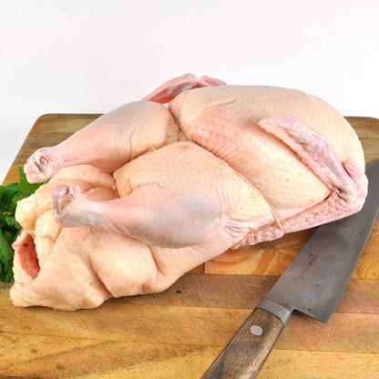 A whole Pekin duck on a wooden cutting board with a knife and some parsley leaves.