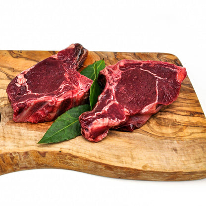 Two raw NZ Venison Rib Chops on a wooden cutting board with a leaf of lettuce.