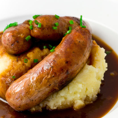 Two sausages on mashed potatoes with gravy on a white plate